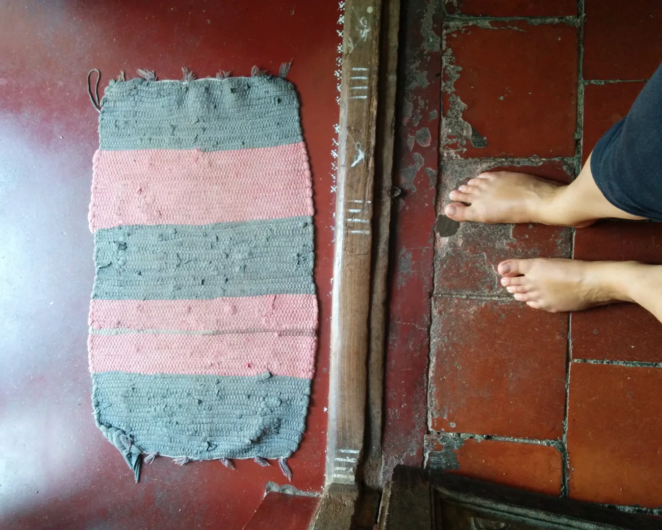 Piedi nudi di Chiara De Servi su pavimento in cotto vicino a un tappetino artigianale, momento simbolico di connessione con la terra.